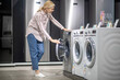 © zinkevych - Woman in striped shirt choosing a washing machine in a showroom