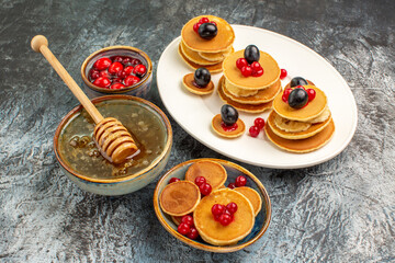 Wall Mural - Top view of classic pancakes on wooden cutting board honey in a white bowl on gray background