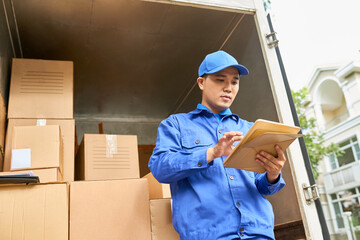 Wall Mural - Serious young Asian courier checking address on tablet computer when deliverying packages and parcels to customer