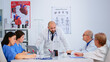 © DC Studio - Professional doctor standing in front of colleagues presenting diagnosis of patients planning treatment development, brainstorming in hospital meeting room. Teamwork research during medical conference