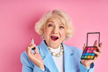 senior lady applying new product cosmetics isolated on pink background, beauty concept