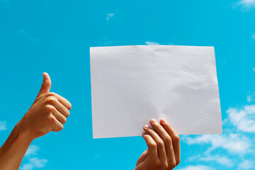 a blank sheet of paper in the hands of a young guy against a blue sky with clouds