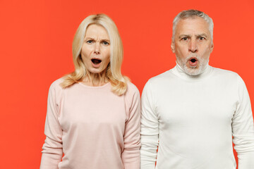 Shocked amazed worried couple two friends elderly gray-haired man blonde woman in white pink casual clothes standing keeping mouth open looking camera isolated on orange background studio portrait.