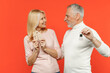 © ViDi Studio - Funny couple two friends elderly gray-haired man blonde woman in white pink casual clothes hold house bunch of apartment keys looking at each other isolated on orange color background studio portrait.