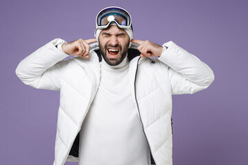 Wall Mural - Crazy skier man in white windbreaker jacket ski goggles mask cover ears with fingers screaming spend extreme weekend winter in mountains isolated on purple background. People lifestyle hobby concept.