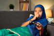 © WESTOCK - Lazy muslim girl kid playing video game by using joystick or gamepad at home while sleeping on sofa at home
