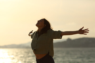 Wall Mural - Silhouette of excited woman stretching arms on the beach