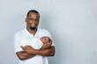 © Ursula Page - An attractive African-American new father is holding his newborn son and looking at the camera with a white-gray background.