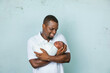 © Ursula Page - An attractive African-American new father is holding his newborn son and looking at him  with affection on a white-gray background.