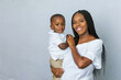 © Ursula Page - A beautiful young African-American woman with braids is holding her toddler age cute son and looking at the camera with a white gray background.