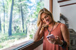 © Javier De La Torre Sebastian/Westend61 - Smiling blond female tourist using smart phone while standing by window at retreat