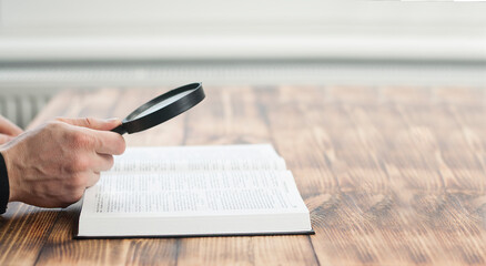 Opened bible book and magnifier in hand. On a wooden table. Research concept