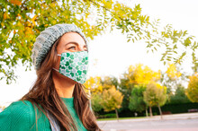 Mature Woman Looking Away While Wearing Protective Face Mask Standing In Public Park On Sunny Day