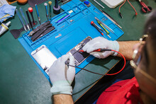 Male Engineer Examining Damaged Smart Phone At Workbench At Repair Shop