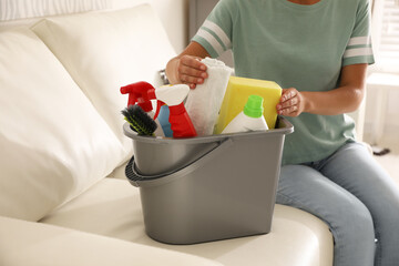 Canvas Print - Woman holding bucket with cleaning supplies in living room, closeup