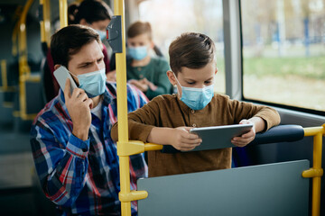 Wall Mural - Small boy using touchpad while commuting by by with his father during coronavirus pandemic.