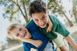 © Mareen Fischinger/Westend61 - Smiling brothers with arm around kneeling in public park on sunny day