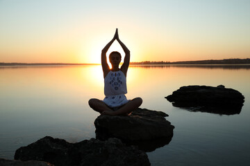 Woman practicing yoga near river on sunset. Healing concept