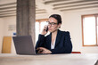 © Westend61 - Businesswoman talking on mobile phone while working on laptop at office