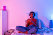 © Giorgio Magini/Westend61 - Teenage girl sitting on bed using smart phone to listen music through headphone at home