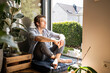 © UWE_UMSTAETTER/Westend61 - Mid adult man sitting on cushion at home on sunny day