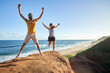 © Veam/Westend61 - Cheerful couple jumping with arms raised on rock formation at beach