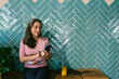 © Xavier Lorenzo/Westend61 - Woman using smart phone while sitting with juice against turquoise wall at bar