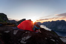 Woman Sitting In Camp On Mountain During Sunset At Reinebringen. Lofoten, Norway
