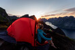 © Matthias Aletsee/Westend61 - Woman admiring view while sitting in camp on mountain at Reinebringen. Lofoten, Norway