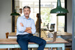 © peter scholl/Westend61 - Confident businessman sitting with arms crossed by laptop on table at office