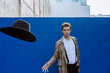 © Xavier Lorenzo/Westend61 - Stylish man wearing checked jacket throwing black hat against blue wall