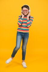 Wall Mural - Correct learning. hipster party fashion style. happy teen girl wear modern headphones. funny kid listen music. beauty in glamour glasses. childhood happiness. smiling child on yellow background