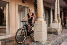 Smiling Woman Looking Away While Standing On Mountain Bike By Pillar On Street