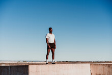 Male Athlete Standing On Wall Against Blue Sky During Sunny Day