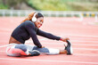 © GERMAN GONZALEZ/Westend61 - Female athlete listening music while doing stretching exercise sitting on runner track