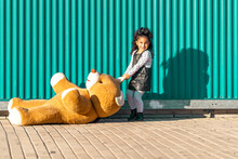 Girl Dragging Teddy Bear On Footpath While Playing Against Green Wall