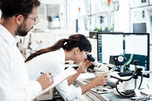 Female Business Professional Looking Through Microscope While Standing By Male Colleague At Laboratory