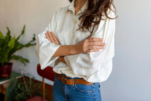 Woman Wearing White Shirt With Arms Crossed Standing Against Wall At Home