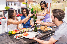 Happy Young Friends Toasting Beer Bottles While Enjoying Brunch At Building Terrace
