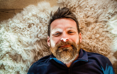 portrait of happy relaxed man laying on sheepskin rug