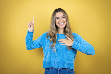 Pretty blonde woman with long hair standing over yellow background smiling swearing with hand on chest and fingers up, making a loyalty promise oath