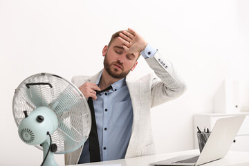 Wall Mural - Man suffering from heat in front of fan at workplace