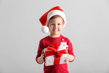 Sticker - Cute little boy in Santa Claus hat holding gift box on light grey background