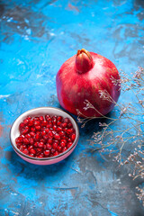 Vertical view of fresh pomegranates and seeds in a white bowl on blue background