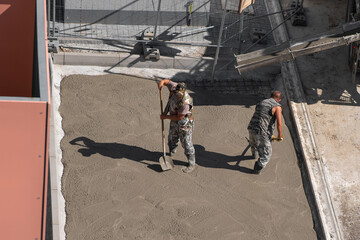 men working on a new concrete driveway at a residential home.Two men are laying concrete on the sidewalk. Renovation work.