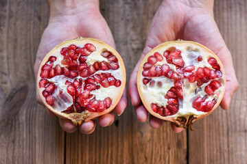 Wall Mural - Pomegranate fruit cut half on hand, ripe pomegranate with seeds on wooden table background.