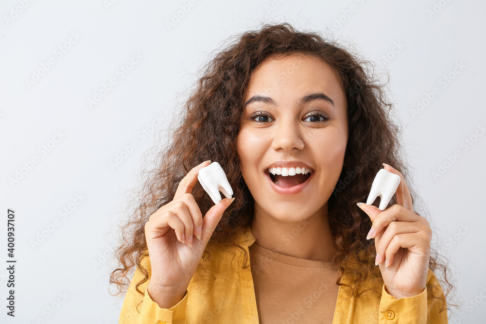 Beautiful young woman with models of teeth on light background