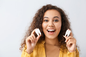 Poster - Beautiful young woman with models of teeth on light background