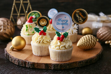 Wall Mural - Board with tasty Christmas cupcakes on dark background