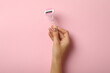 Female hand hold razor on pink background, space for text